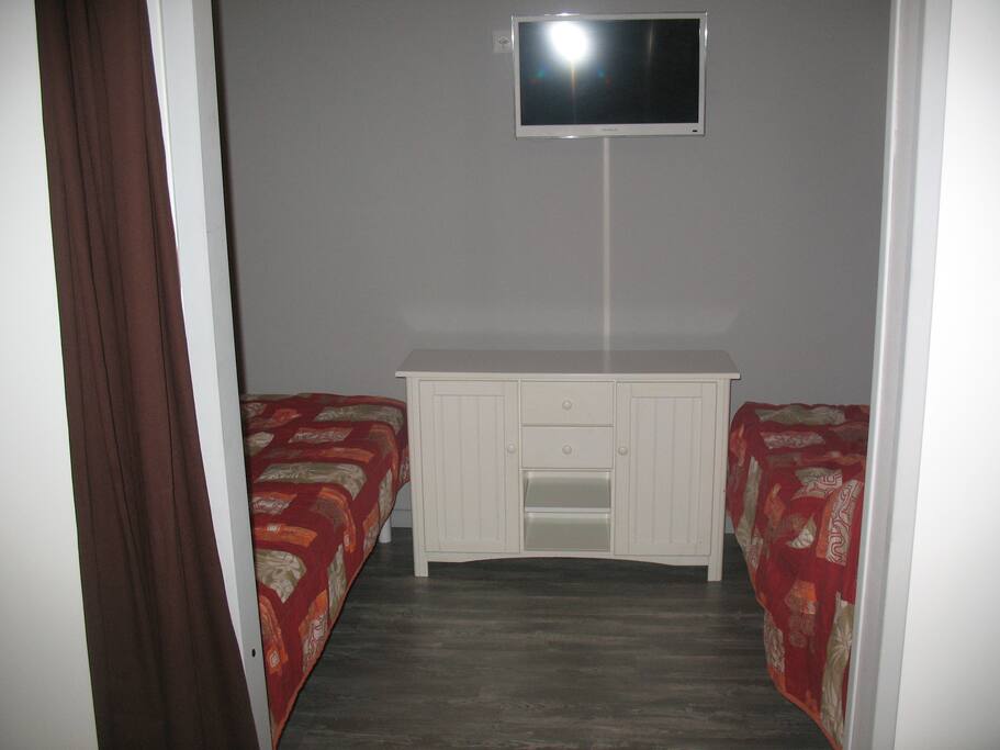 2 lits séparés avec une télévision centrale, d'une commode aux pieds et 2 bacs de rangement sous les lits. 2 têtes de lits avec étagères et portes téléphone avec prises électriques.