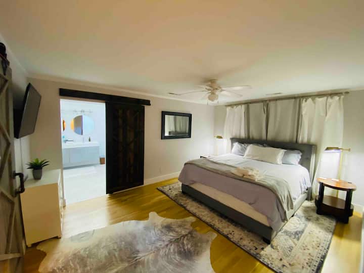 Recámara principal con cama tamaño king, televisor inteligente de 50 pulgadas, pisos de madera y acceso privado al baño principal en esta casa de vacaciones de Mount Pleasant.