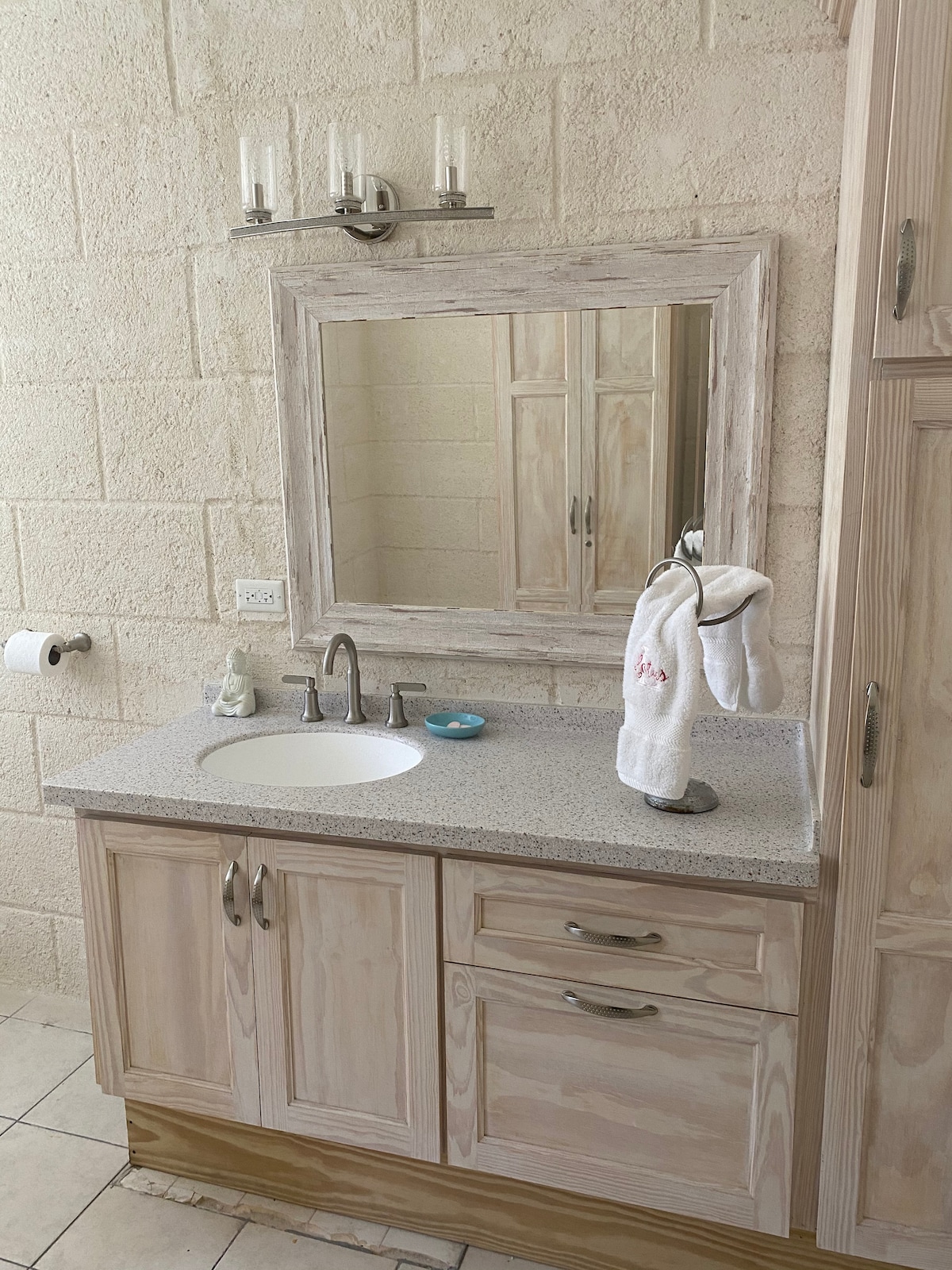 A modern bathroom features a light wood vanity with a speckled countertop. A round sink is integrated into the surface, accompanied by a polished chrome faucet. A large mirror hangs above the vanity, framed in matching wood. Towels are elegantly displayed on a towel holder.
