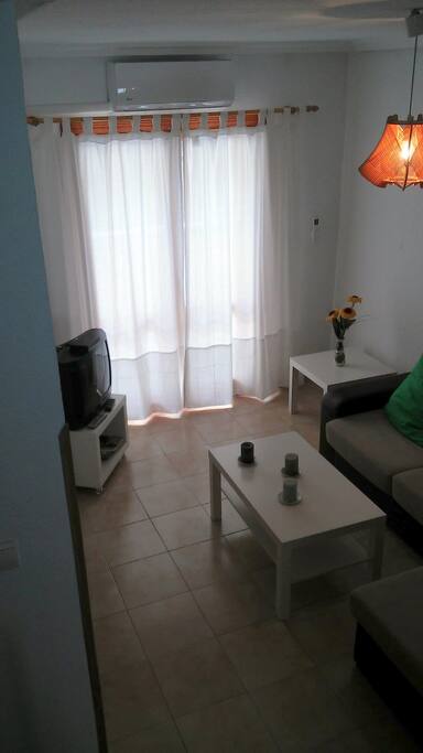 Salón con sofá con chaiselonge, TV, aire acondicionado, mesa y sillas