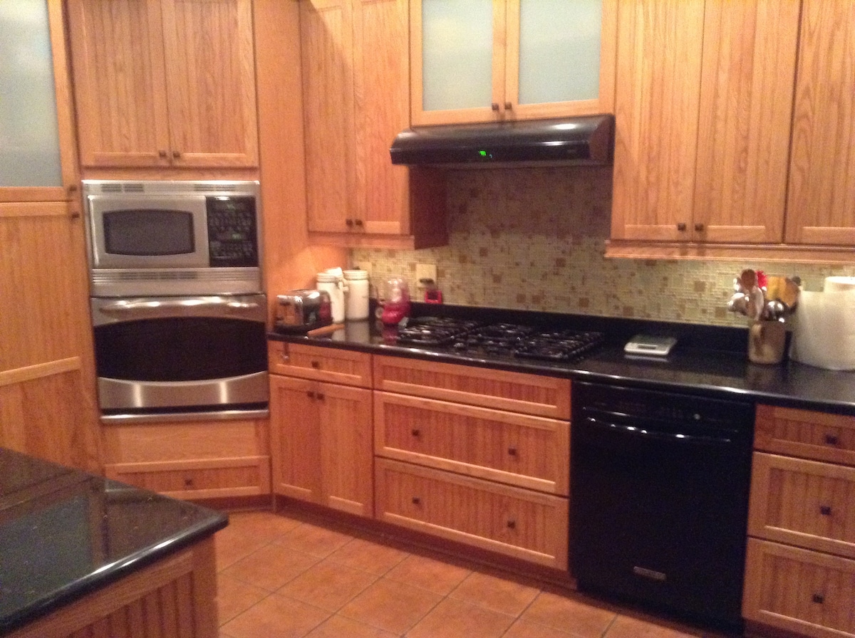 A well-appointed kitchen features wooden cabinetry and dark countertops. Appliances include a built-in oven, a gas cooktop, and a dishwasher. Soft lighting reflects off the tiled backsplash, while organized kitchenware is visible on the counters, enhancing the functional layout.
