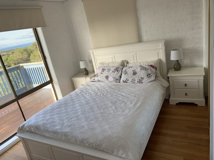 Dormitorio en la planta superior con traje de estilo provincial queen y puertas con espejos incorporadas, suelos de madera con vistas al mar.