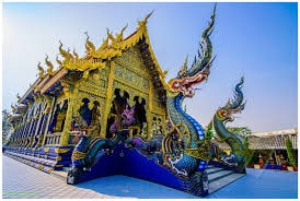 An intricately designed temple facade is depicted, featuring ornate golden roofs and colorful dragon sculptures. The vibrant blue and gold elements create a stunning contrast against the clear sky, highlighting the architectural details and craftsmanship of the structure.