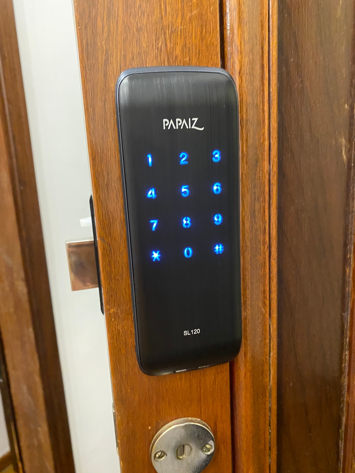 An electronic lock is displayed on a wooden door, featuring a lighted keypad with numerical buttons. The sleek design complements the door's natural finish, and a keyhole is visible below the keypad, providing a modern security feature for guests.