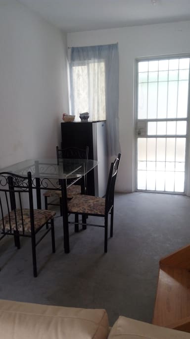 Ante comedor tubular con 4 sillas y mesa de vidrio. Área de cocina con refrigerador, estufa, tarja y trastos necesarios