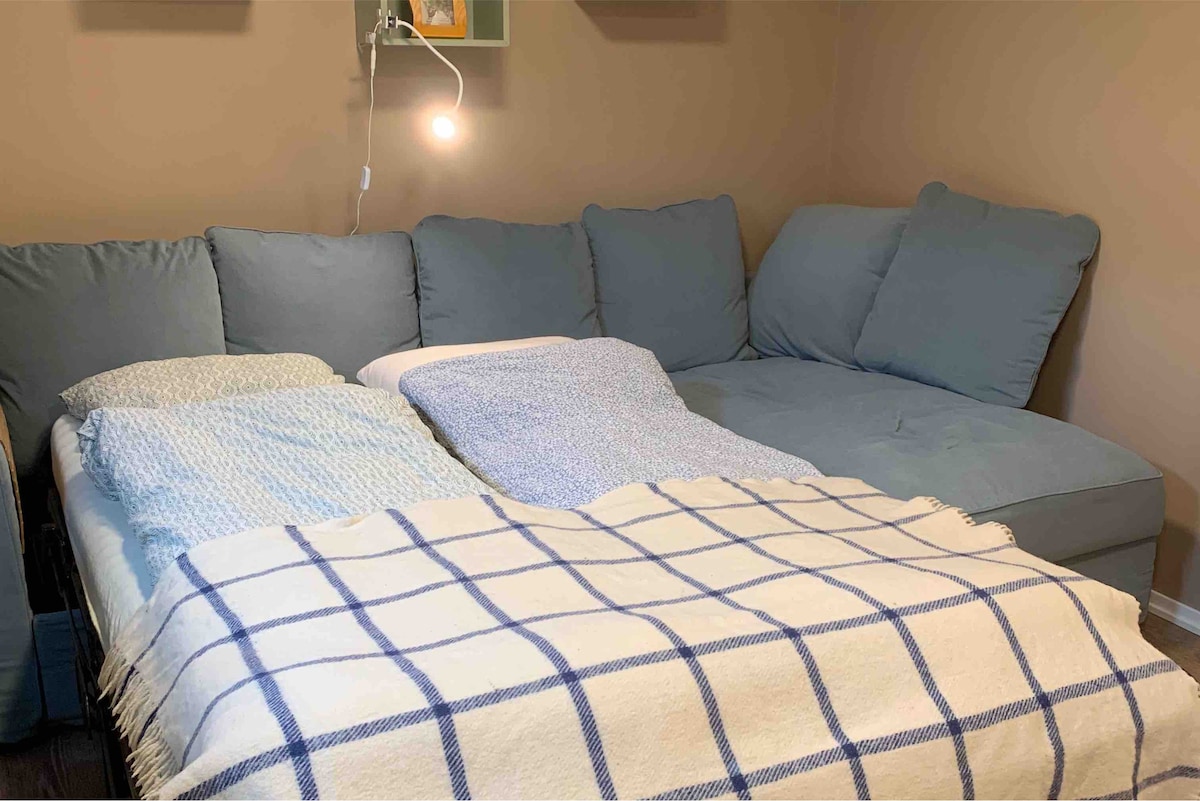 A comfortable sleeping area is highlighted by a spacious couch that converts into a bed. Soft blankets are layered over the bed, with a cozy texture adding warmth. A reading light is mounted on the wall, providing illumination for evening relaxation.