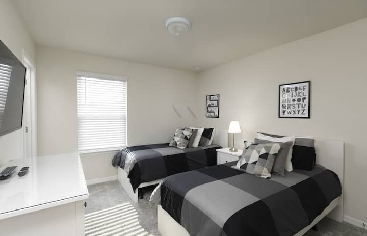 ¡Un refugio elegante y cómodo! Esta habitación secundaria con dos camas individuales cuenta con dos camas vestidas con una llamativa ropa de cama a cuadros geométricos en gris carbón, decorada con impresiones gráficas monocromáticas en la pared y una mesita de cabecera compartida.