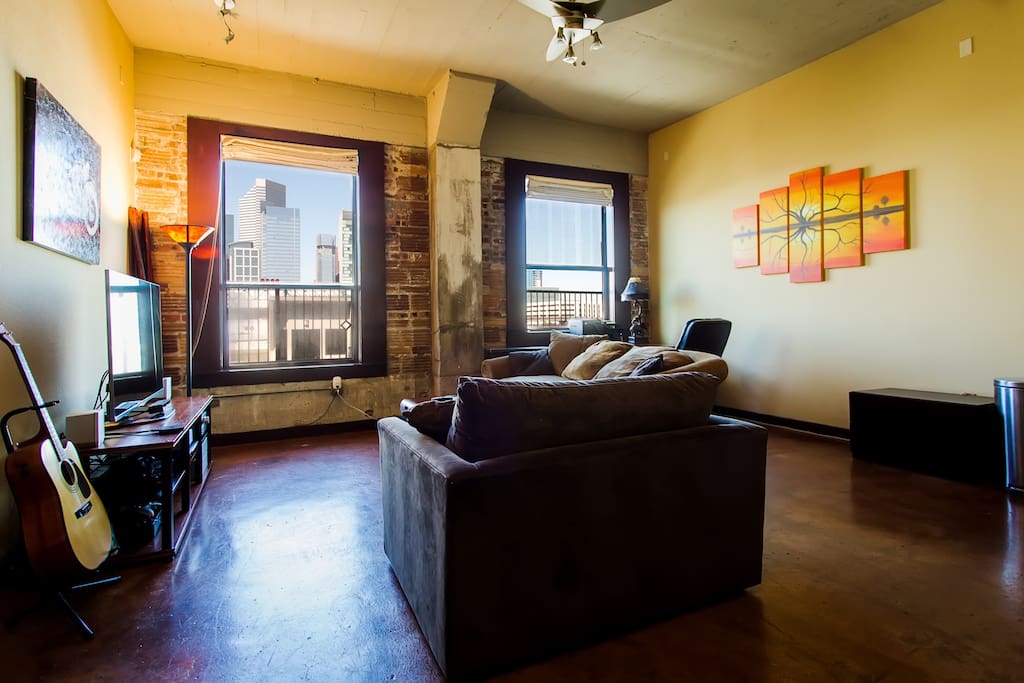 Spacious living room with exposed brick, high ceilings, concrete floors, and an incredible view of downtown Houston.