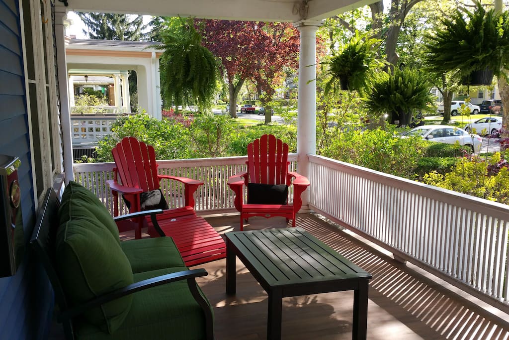 Guests enjoy time on the front porch. The house is on a tree lined street.
