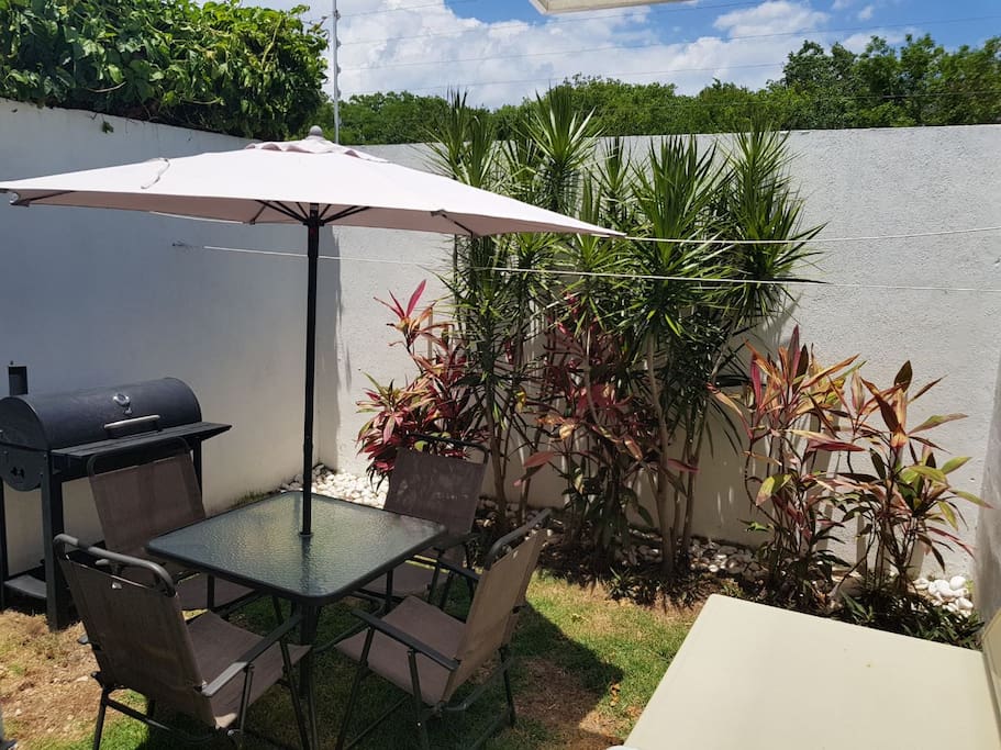 Jardín interior de casa, mesa con sombrilla y con asador