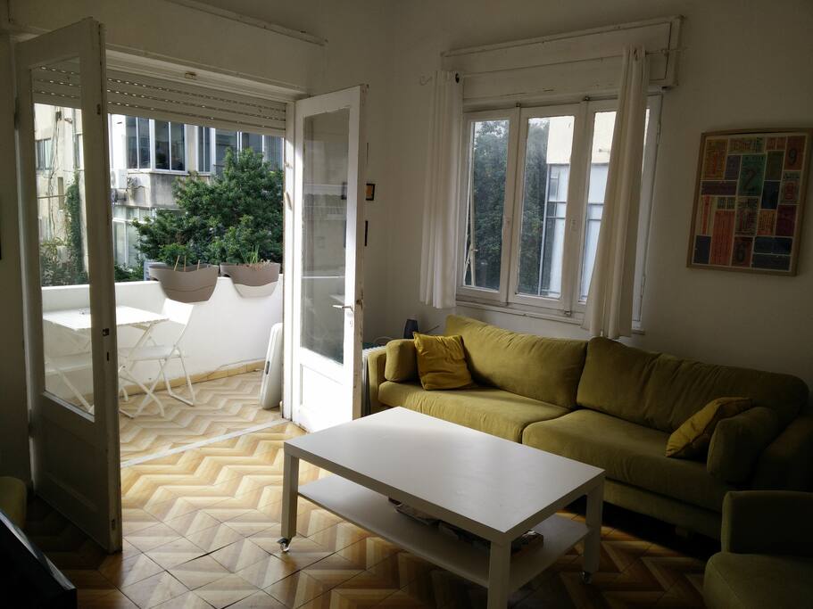 The living room allows access to a street view balcony with a table and chairs.