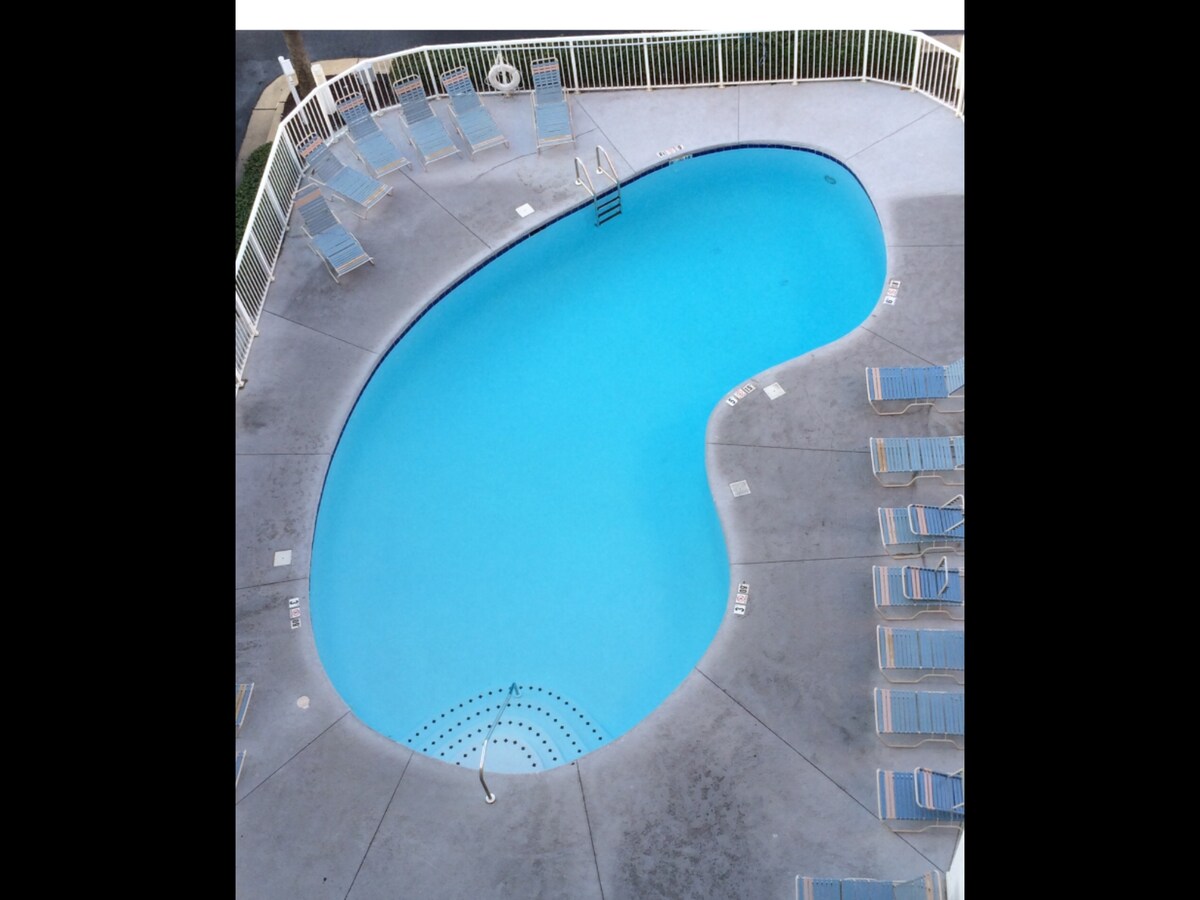 A private pool is shown, featuring a unique organic shape accented by blue water. Surrounding the pool are multiple lounge chairs arranged neatly along the concrete deck, providing space for relaxation and sunbathing.