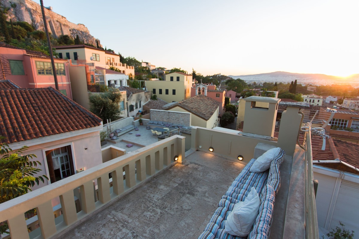A spacious terrace is shown with comfortable seating and city views at sunset. The scene captures rooftops and distant hills, highlighting the warm colors of dusk. Soft outdoor lighting creates an inviting ambiance, complementing the surrounding architecture.