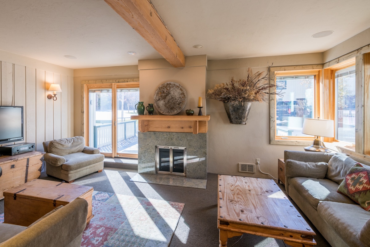 A bright living area features large windows providing ample natural light. A stone fireplace acts as a focal point, complemented by cozy seating options. Decorative items, such as a wall-mounted planter and various furnishings, enhance the inviting atmosphere.