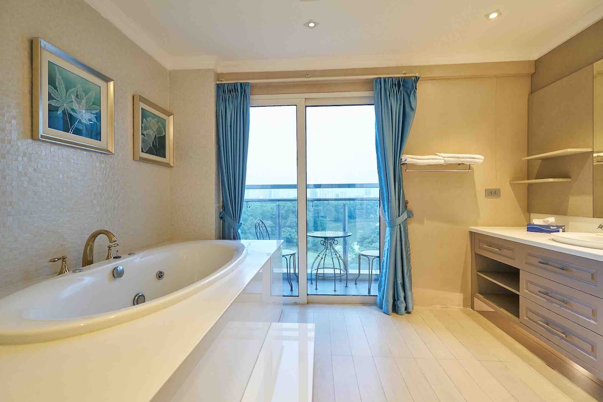 A spacious bathroom is equipped with a freestanding bathtub and a modern vanity with ample counter space. Natural light filters through sliding glass doors, which lead to a small balcony. Elegant artwork adorns the walls, complementing the serene atmosphere.