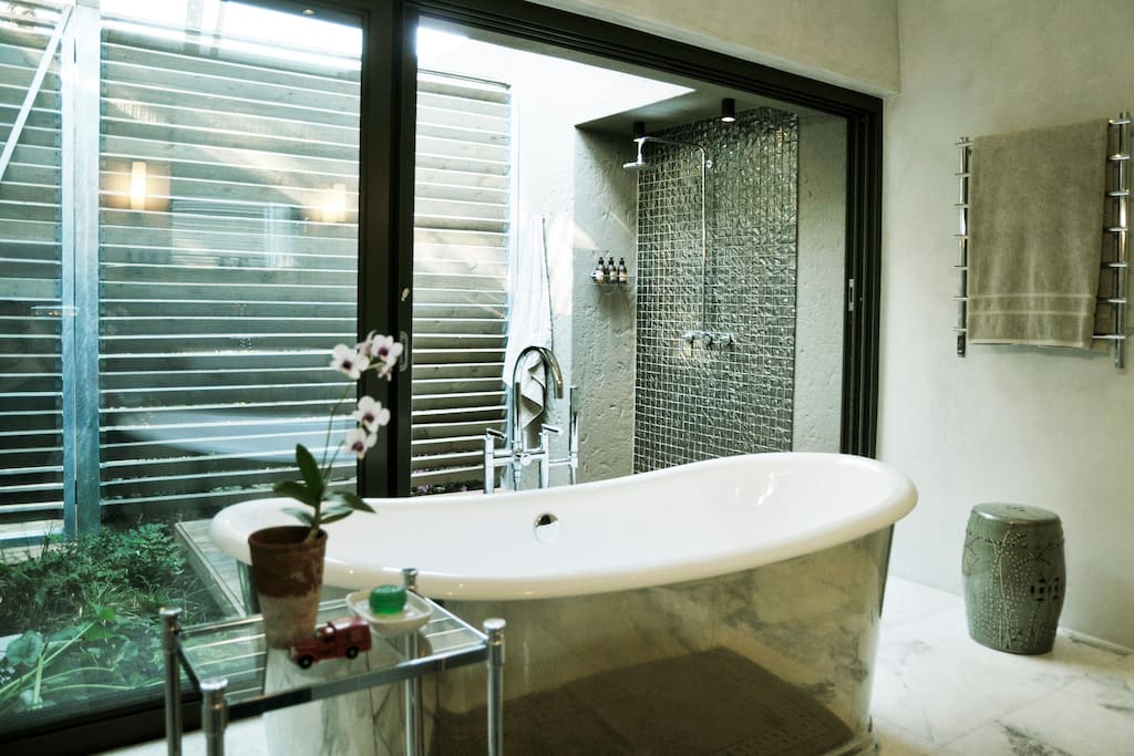 Luxurious bathroom featuring a freestanding pewter bath and an outside shower within an enclosed tropical courtyard.