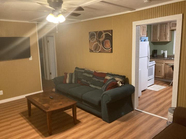 WELCOME TO OUR TOUR! This is the living room with access to a small kitchen and laundry room. Bedrooms and bathroom can be accessed to the right. Main door entrance is on the right next to the TV. 