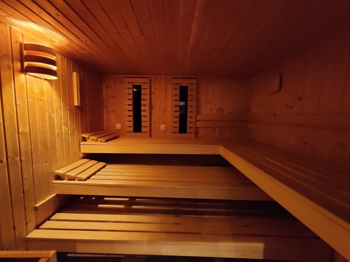 A wooden sauna interior is depicted, featuring bench seating arranged on two sides. The walls are paneled with smooth wood, and soft lighting creates a warm atmosphere. Ventilation openings are visible near the ceiling, contributing to the space's functionality.
