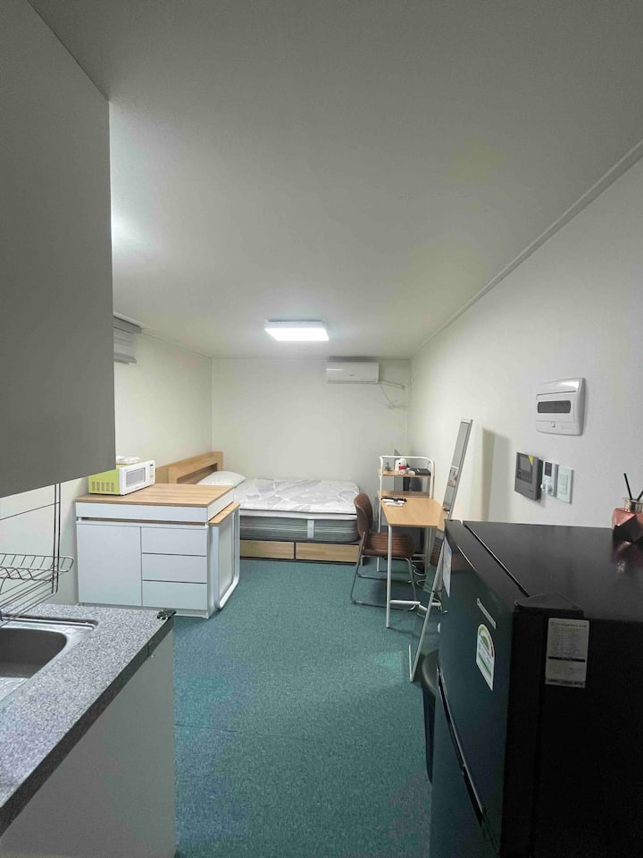 Това е снимка на целия интериор на мястото за настаняване.
Има мивка, бюро, огледало, маса за хранене, телевизор и двойно легло.