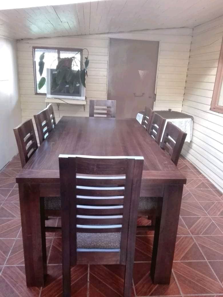A dining area is displayed with a large rectangular table made of dark wood, surrounded by eight matching chairs. Natural light enters through two windows, enhancing the space's inviting feel. The floor features a distinctive tile pattern, complementing the room's overall design.