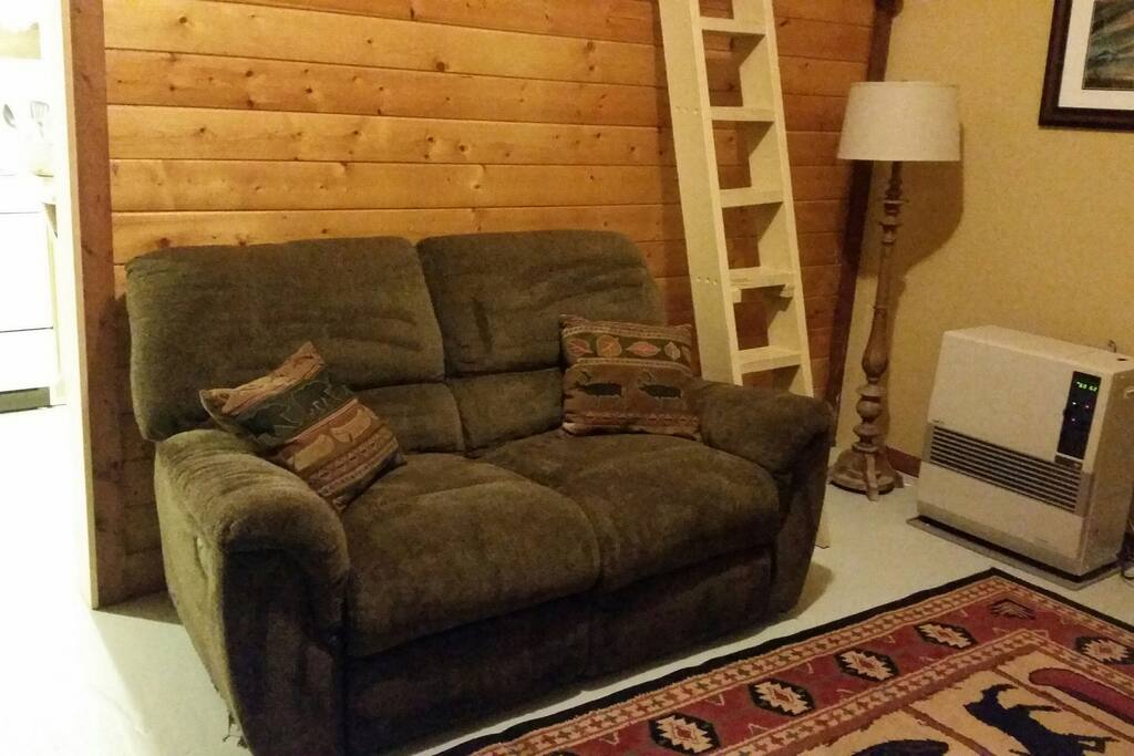 Soft, reclining loveseat, with Toyo stove (heater), and flat screen television with Dish Network opposite loveseat (television not visible in photo) . . .