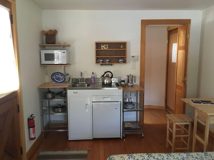 Studio kitchenette (with stovetop, sink, mini-fridge, microwave and tea/coffee-makers), open table and hallway to full bath
