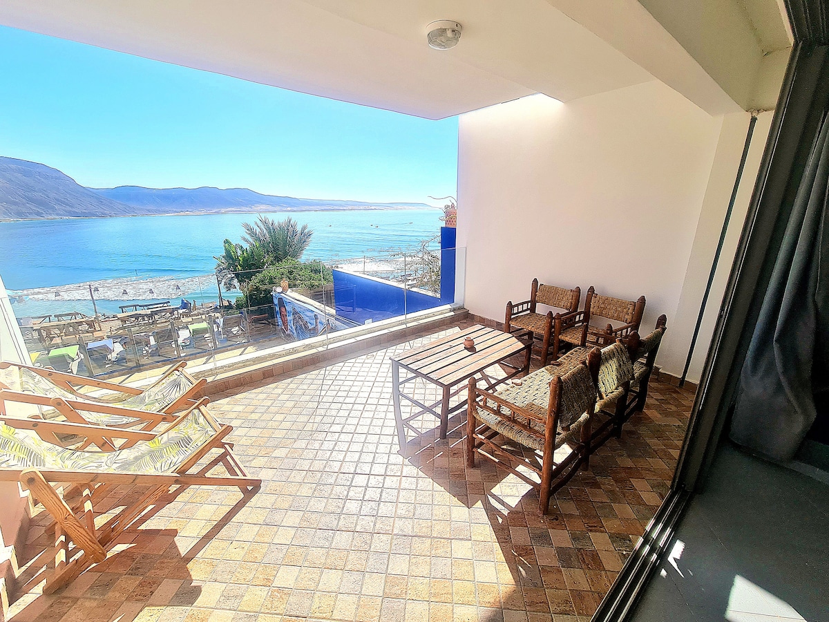 A private terrace offers panoramic views of the sea and surrounding landscape. Comfortable seating is arranged on a tiled surface, complemented by loungers. The outdoor area is designed for relaxation, inviting guests to enjoy the serene environment.