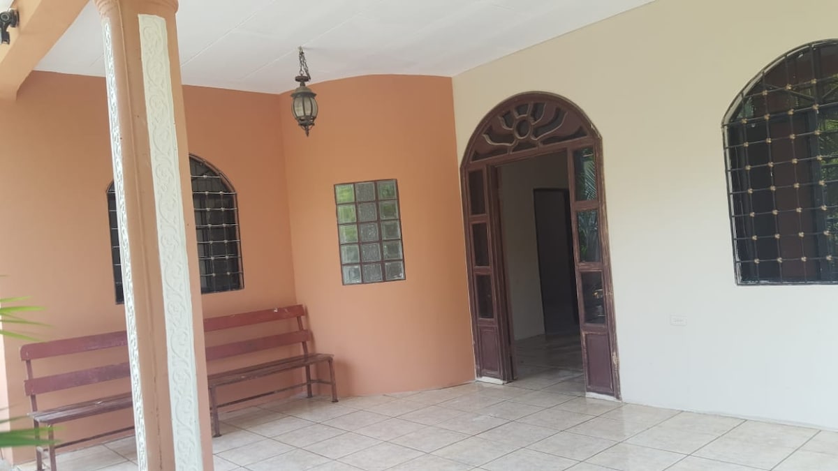 A welcoming entryway is featured, showcasing two arched doorways leading to additional spaces. A wooden bench is positioned against a wall, complemented by decorative glass block windows. The tiled floor provides a clean and open feel, while natural light flows into the area.