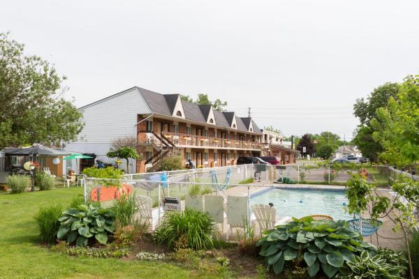 The outdoor area features a well-maintained pool surrounded by lush green landscaping. A two-story building with balcony access sits in the background, providing a view of the surrounding foliage and amenities.