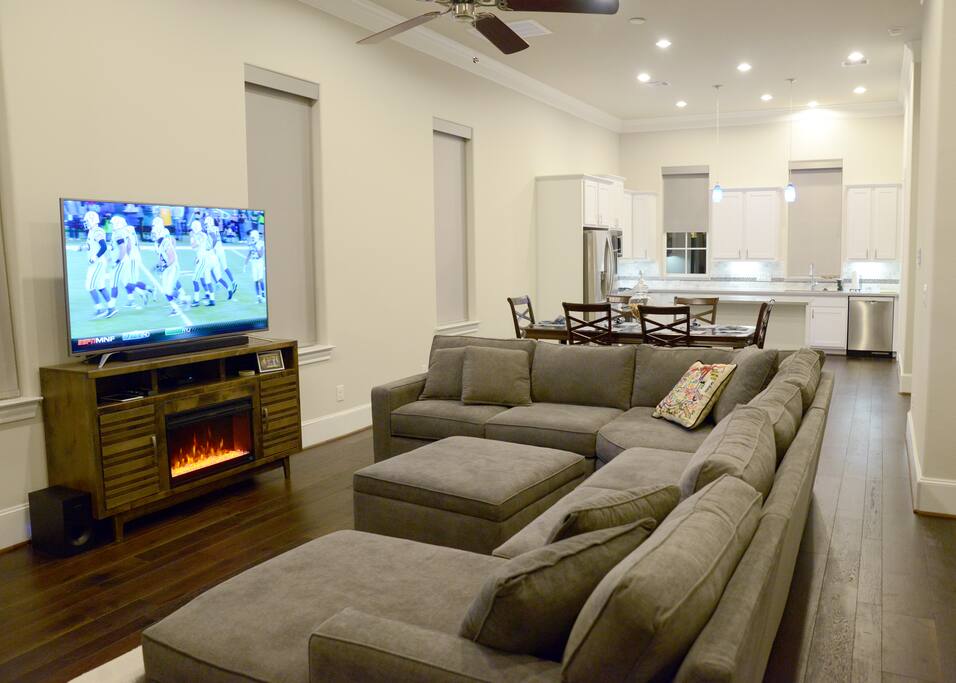 This is a closer view of the living room. There is a 65 inch 4d TV and sound bar. And a faux fireplace.