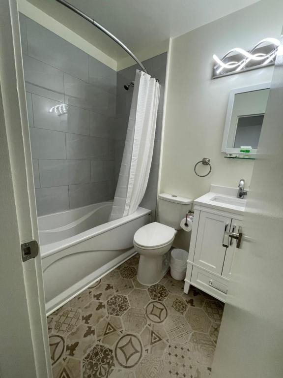 A clean bathroom is presented, featuring a bathtub with a shower curtain and sleek tile walls. A compact vanity with a sink is positioned beside a modern mirror. Decorative tiles cover the floor, contributing to the overall contemporary design.