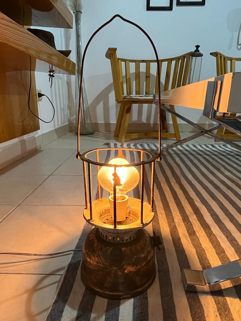 A decorative lantern stands on the floor, featuring a warm bulb encased in a wire frame. In the background, a wooden chair is visible, complementing the striped rug and light-colored tiles.