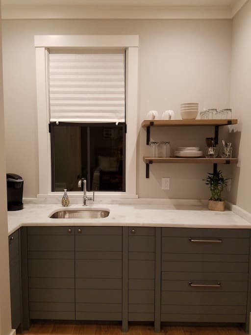 Kitchenette with natural marble countertop, fridge/freezer, Keurig coffee maker, microwave and dishes