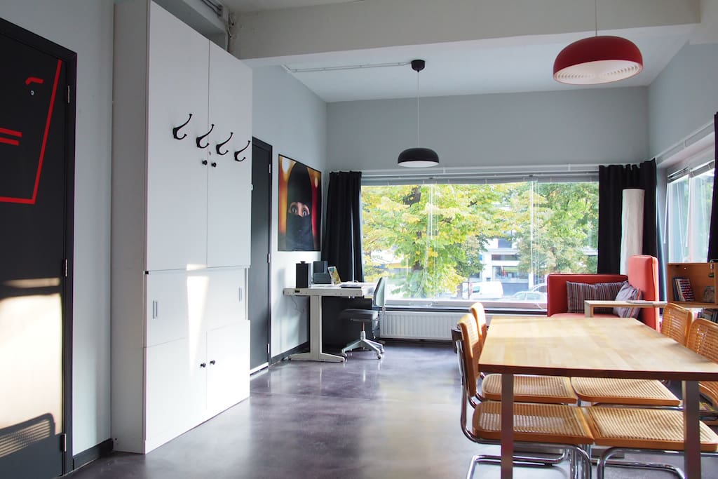 The main living space viewed from the opposite side with the dining table, the small sofa and the working desk and chair. The main entrance door is on the far left.