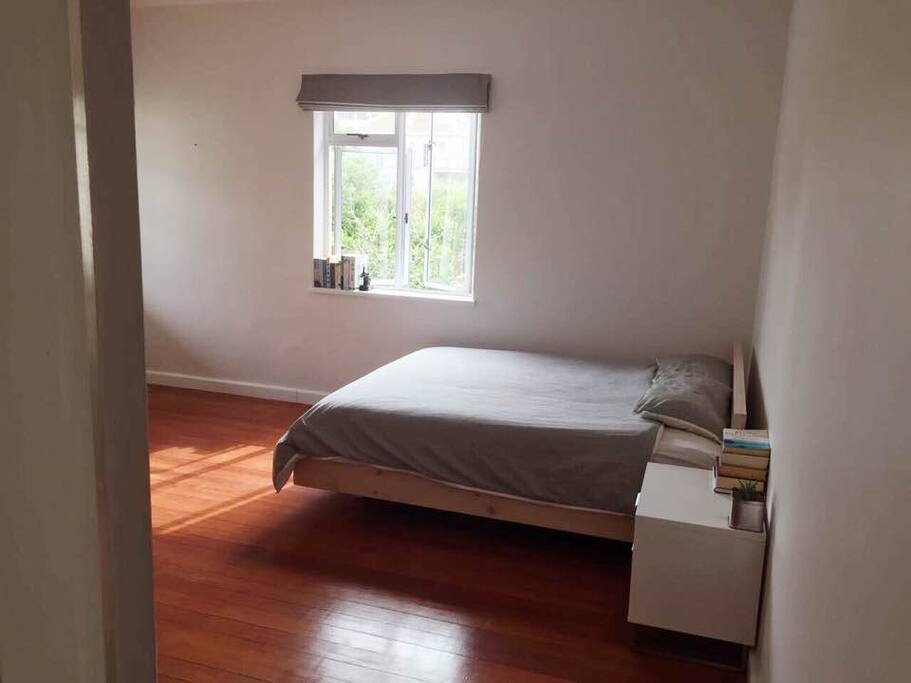 The bedroom: view of the sunny space with queen-sized bed and bedside table.