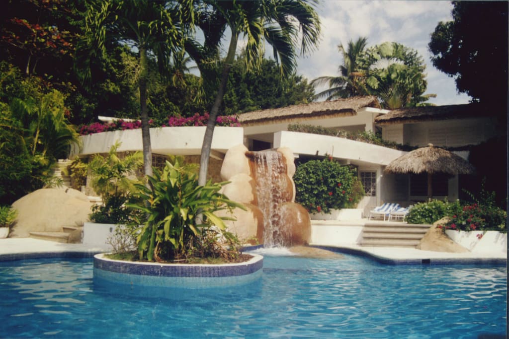 LOWER LEVEL POOL WITH AN ARTIFICIAL CASCADE AND ISLAND WITH TWOO PALM TREES.