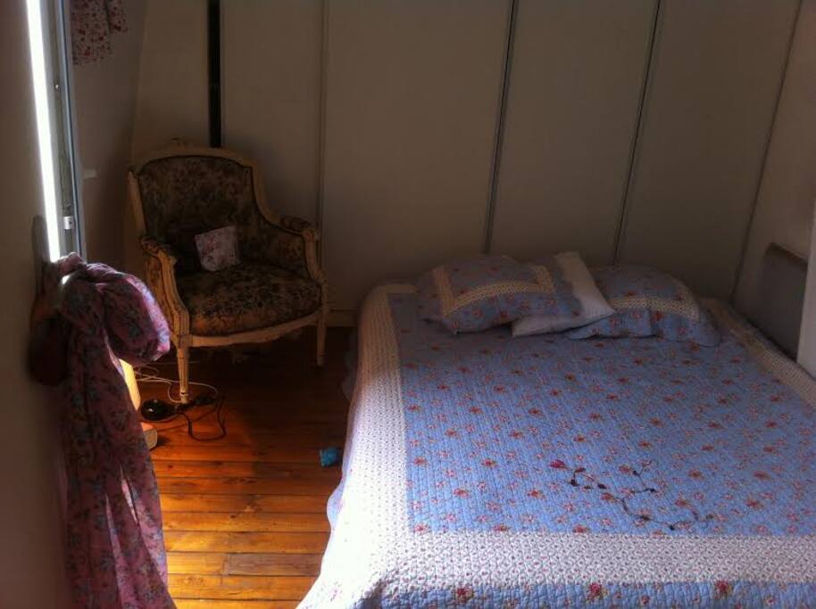 La chambre pour deux personnes avec parquet au sol, grande fenêtre, fauteuil d'époque, bureau en bois d'époque. Ambiance liberty parisienne.