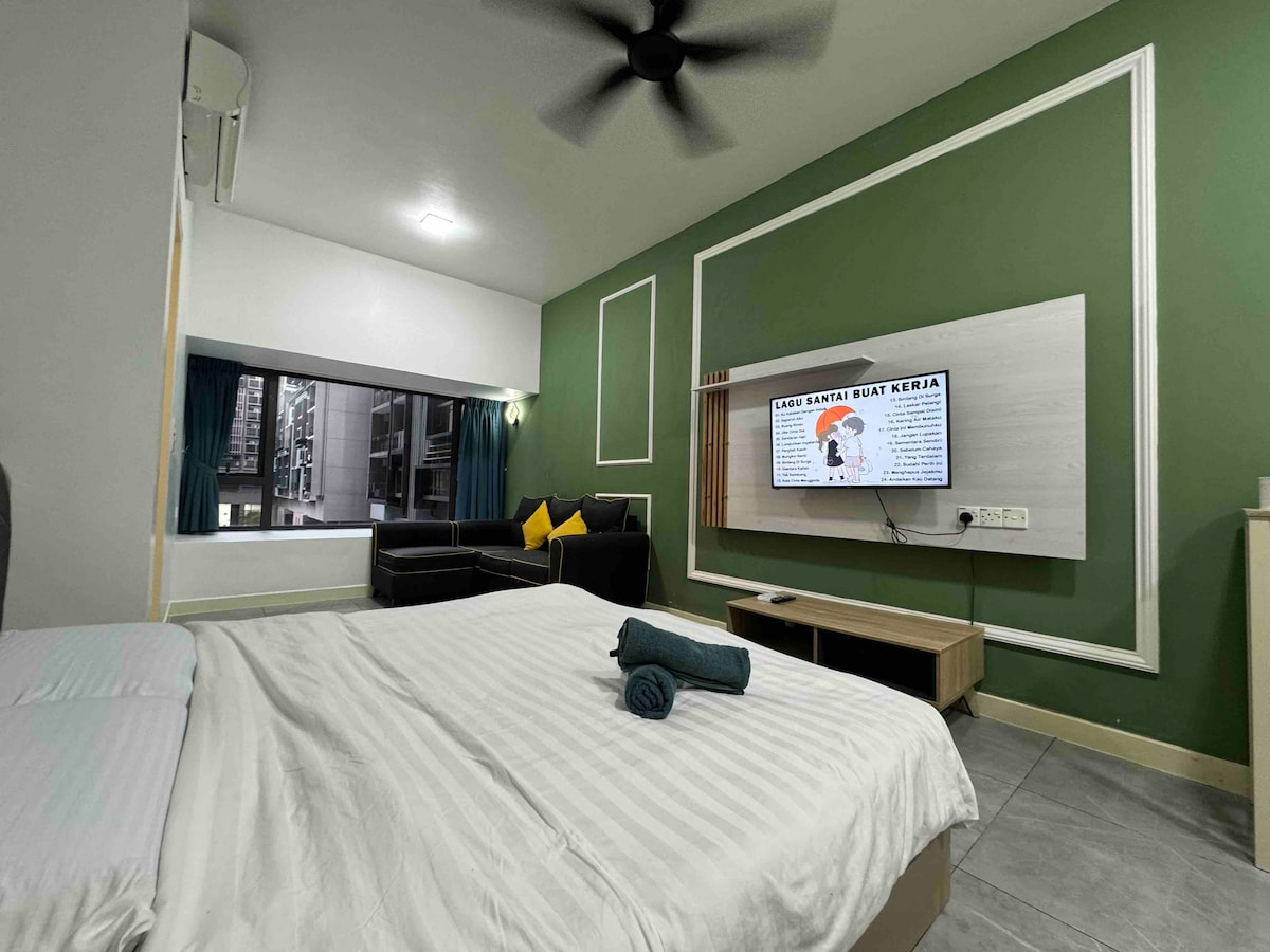 The spacious studio unit features a comfortable king size bed with a neatly arranged blanket. A large window offers views of the surroundings, while a stylish sofa and a smart TV are also present. Air conditioning is available for comfort.