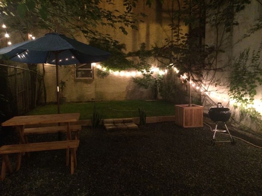 Backyard at night with BBQ, fire pit, picnic table, umbrella and lights (Fair warning: Plants died over the winter)
