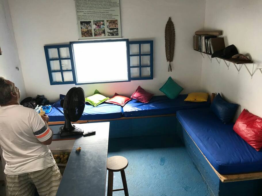 Espaço comum com três sofás de alvenaria sendo que o da direita transforma em uma cama de casal.