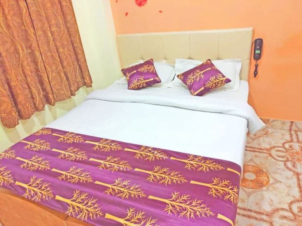 A well-furnished sleeping area features a spacious bed adorned with vibrant bedding and decorative pillows. The walls are painted in a warm orange hue, complemented by patterned curtains. A telephone is mounted on the wall beside the bed.