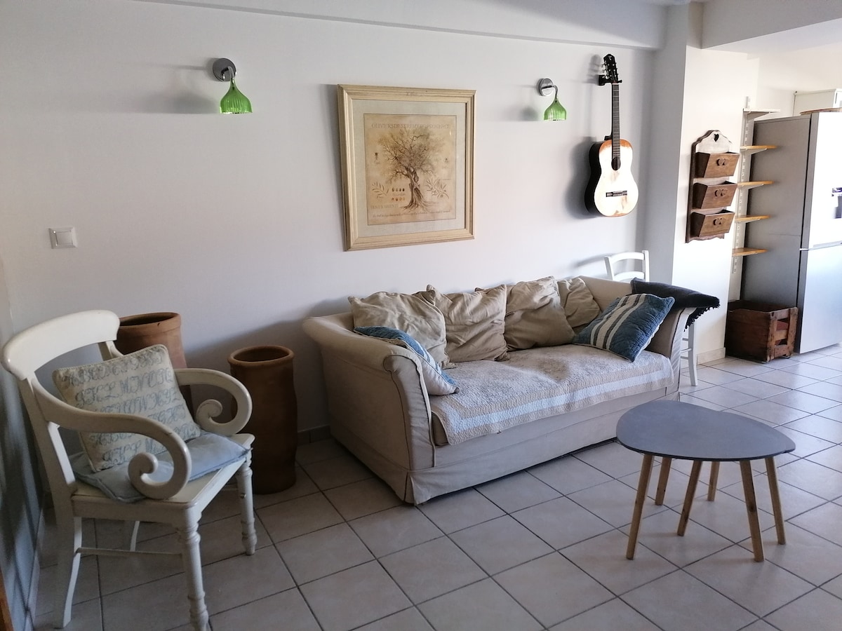 The living area displays a light-colored sofa with decorative cushions, complemented by a small round coffee table. A guitar hangs on the wall, and warm light is provided by green pendant lamps. Storage options are visible, along with tiled flooring.