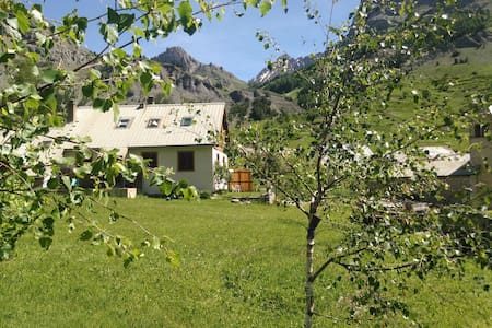 A spacious outdoor area showcases a well-maintained grassy lawn surrounded by mountain scenery. The building features a light-colored facade with a sloped roof, blending into the natural surroundings. Trees provide a sense of tranquility, while sunlight brightens the landscape.
