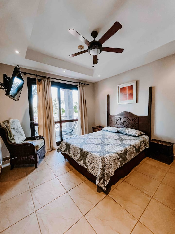 Segundo dormitorio; cama queen y balcón con vistas parciales al mar y asientos. 