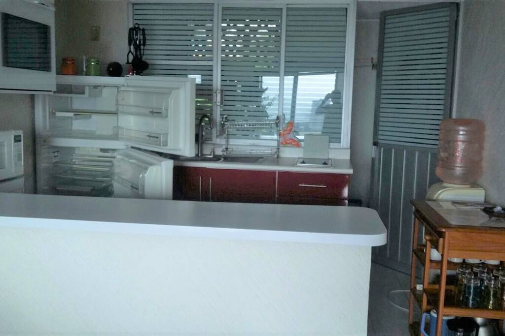 Cocina con refrigerador, estufa eléctrica, horno de microondas, en la parte de atrás zotehuela con lavadora y espacio para colgar ropa