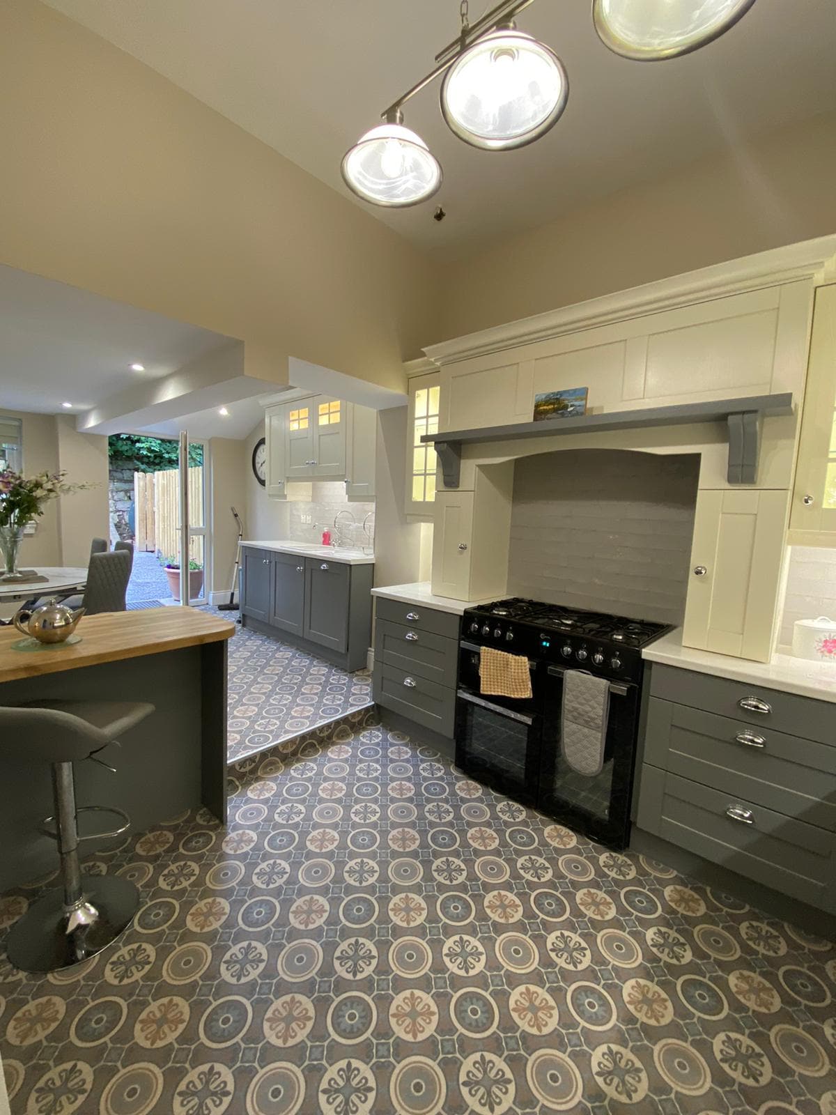 A contemporary kitchen area features dark cabinetry combined with light countertops. A gas stove is positioned against a stylish tiled backsplash. Seating is available at a bar-style counter, and patterned flooring adds visual interest to the space. Natural light is filtered through the adjacent windows.
