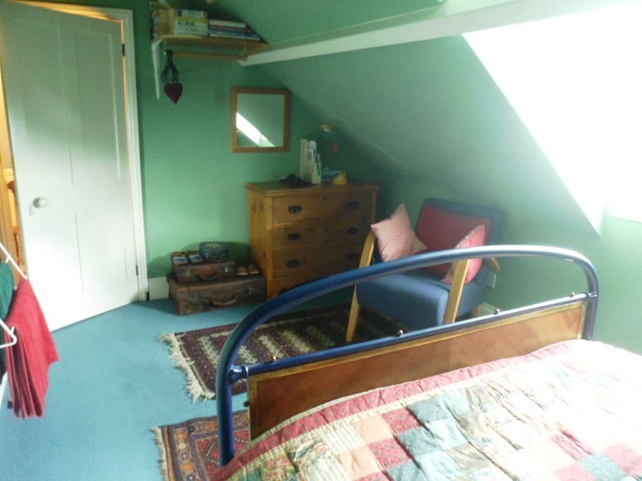 View to door from bed. Drawers and a hanging rail for clothes. Comfy chair.