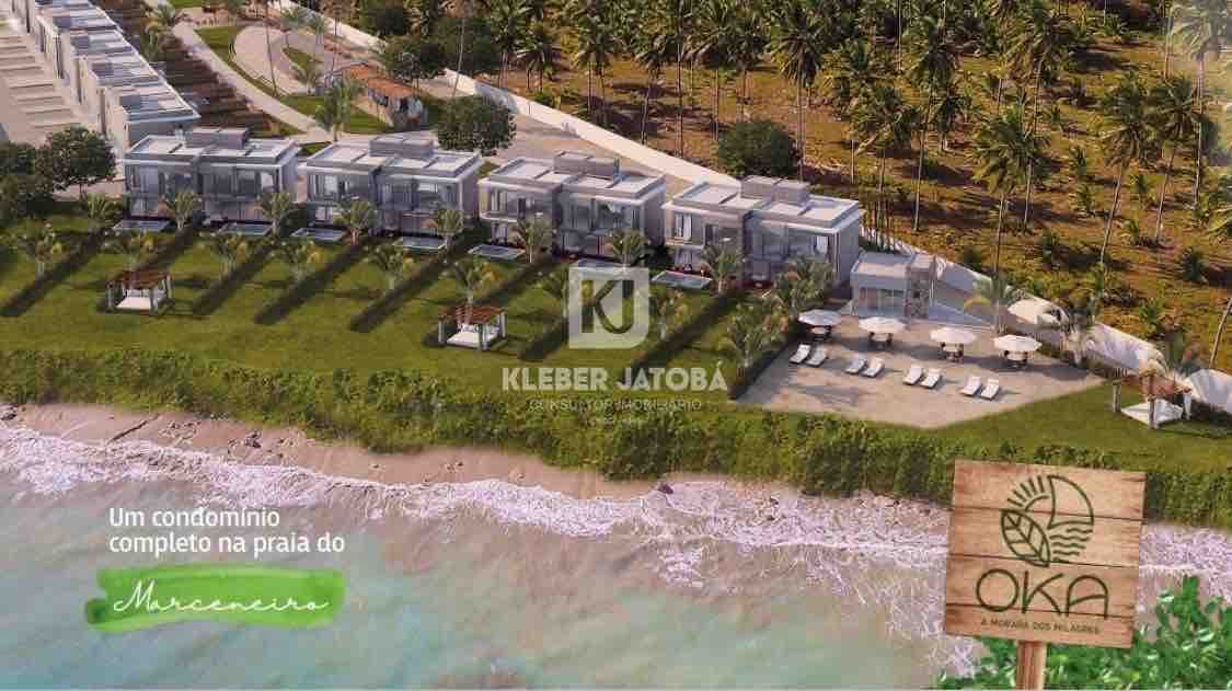 Aerial view of a beachside condominium, featuring a series of modern houses aligned near the shoreline. Sun loungers and umbrellas are positioned on the grassy area, with waves gently lapping at the beach in the foreground.