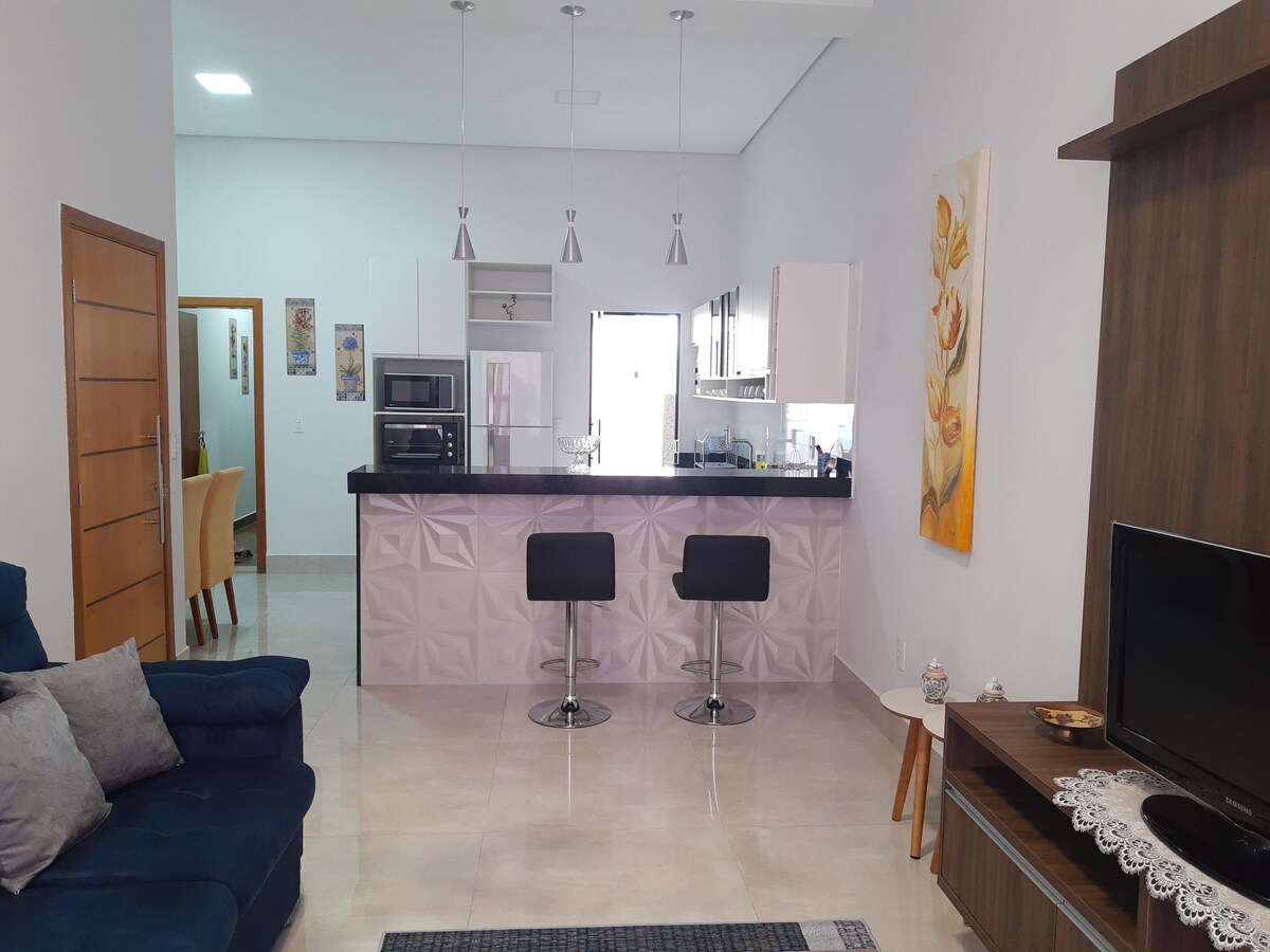 A modern living area features a blue sofa and a sleek kitchen island with two black bar stools. The kitchen is equipped with stainless steel appliances and elegant cabinetry. Natural light fills the space, creating a bright and welcoming environment.