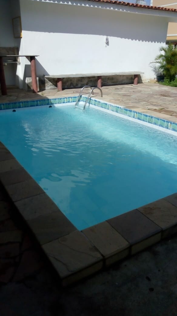 A clear swimming pool is seen, featuring steps for easy access. The poolside is surrounded by natural stone tiles, and a shaded area is available nearby. Sunlight reflects off the water's surface, creating a serene atmosphere.